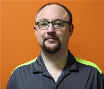 A man in a gray shirt standing in front of an orange background