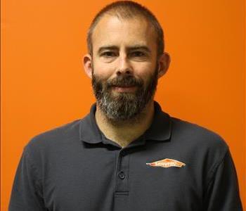 A man in a gray shirt standing in front of an orange background