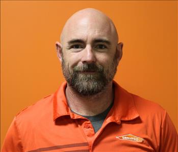 A man in an orange shirt standing in front of an orange background