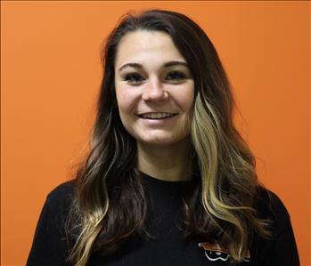 A woman in a black shirt standing in front of an orange background