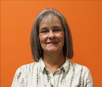 A woman in a white shirt standing in front of an orange background