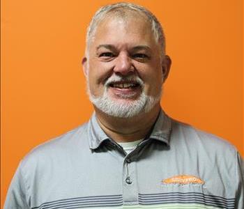 A man in a gray shirt standing in front of an orange background