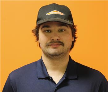 A man in a black shirt standing in front of an orange background