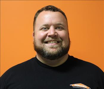 A man in a black shirt standing in front of an orange background