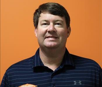 A man in a blue shirt standing in front of an orange background